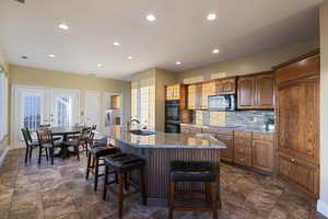 Kitchen with black appliances, a sink, a kitchen bar, recessed lighting, and a center island with sink