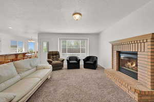 Carpeted living area featuring a chandelier, a brick fireplace, and a textured ceiling