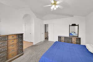 Bedroom featuring light colored carpet, vaulted ceiling, arched walkways, a ceiling fan, and baseboards