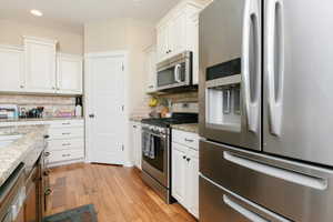 Kitchen featuring appliances with stainless steel finishes, light wood-style floors, white cabinetry, backsplash, and recessed lighting