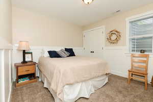 Carpeted bedroom with a wainscoted wall, a closet, and a decorative wall