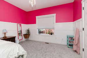 Carpeted bedroom with a decorative wall, a wainscoted wall, and a chandelier
