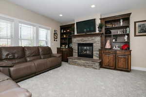 Living room with light carpet, a stone fireplace, recessed lighting, and baseboards