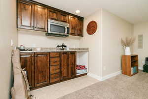 Kitchen with stainless steel microwave, baseboards, light stone countertops, and light carpet