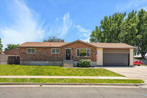Ranch-style home with a garage, concrete driveway, and brick siding. Grass edited in this photo, seed has been planted.