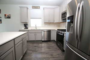 Kitchen featuring appliances with stainless steel finishes, a sink, gray cabinetry, dark wood-style floors, and light countertops