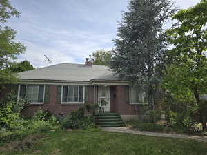 Bungalow-style home featuring brick siding, a chimney, and roof with shingles