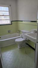 Bathroom with tile patterned flooring, a bath, toilet, tile walls, and wainscoting