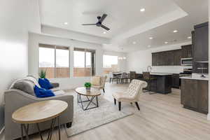 Living room with a tray ceiling, a ceiling fan, light wood-type flooring, recessed lighting, and a chandelier