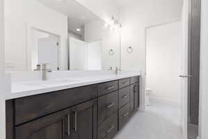 Bathroom featuring double vanity, toilet, and baseboards