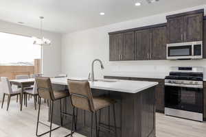 Kitchen with appliances with stainless steel finishes, a sink, a breakfast bar area, light countertops, and dark brown cabinetry