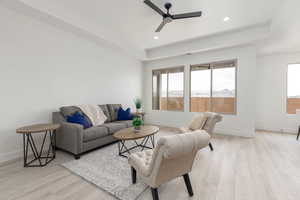 Living room with healthy amount of natural light, a ceiling fan, light wood-style floors, a tray ceiling, and recessed lighting