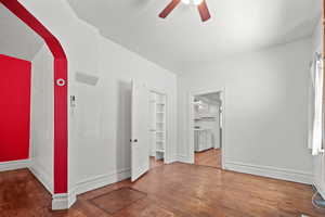 Empty room with a ceiling fan, wood finished floors, independent washer and dryer, arched walkways, and baseboards