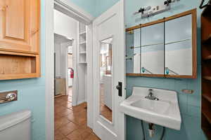 Bathroom featuring toilet, a sink, tile patterned flooring, and tile walls