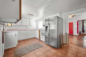 Kitchen featuring stainless steel refrigerator with ice dispenser, electric range, light tile patterned floors, light countertops, and white cabinetry