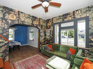 Living room featuring wallpapered walls, wood finished floors, ceiling fan, baseboards, and arched walkways
