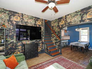 Living area with wallpapered walls, stairway, wood finished floors, a chandelier, and a ceiling fan