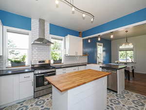 Kitchen with stainless steel appliances, wall chimney exhaust hood, a sink, a peninsula, and butcher block countertops