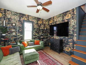 Living room featuring stairs, wallpapered walls, wood finished floors, and ceiling fan