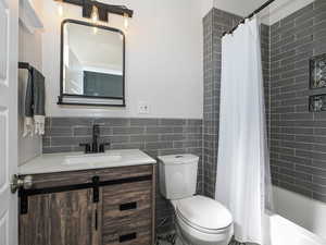 Full bath with vanity, toilet, tile walls, shower / tub combo with curtain, and a wainscoted wall