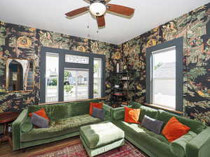 Living area with wallpapered walls, plenty of natural light, a ceiling fan, and wood finished floors