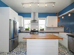 Kitchen featuring stainless steel appliances, wooden counters, wall chimney exhaust hood, and a sink