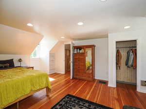 Bedroom with baseboards, wood-type flooring, recessed lighting, vaulted ceiling, and a walk in closet