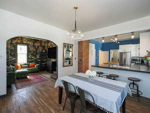 Dining space featuring dark wood-style floors, arched walkways, and a chandelier