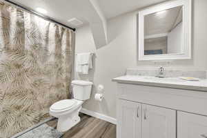 Bathroom featuring toilet, vanity, wood finished floors, baseboards, and curtained shower