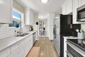 Kitchen featuring appliances with stainless steel finishes, a sink, white cabinetry, and backsplash