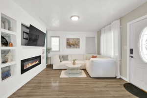 Living room with a glass covered fireplace, a textured ceiling, wood finished floors, built in features, and baseboards