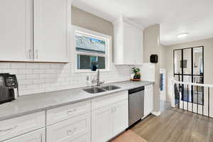Kitchen featuring stainless steel dishwasher, a sink, light wood finished floors, white cabinets, and tasteful backsplash