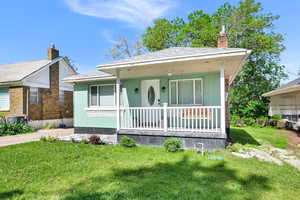 Bungalow-style home featuring covered porch, a chimney, and a front lawn