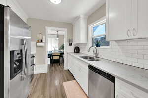 Kitchen with stainless steel appliances, a sink, light wood-style floors, white cabinets, and decorative backsplash