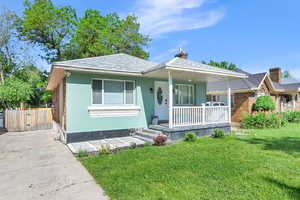 Bungalow-style house featuring covered porch, a front lawn, a chimney, driveway, and a gate