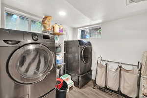 Laundry area featuring washing machine and clothes dryer, wood finished floors, a textured ceiling, and baseboards
