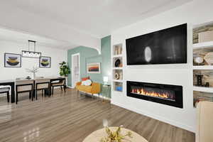 Living area with a glass covered fireplace, wood finished floors, built in shelves, and baseboards