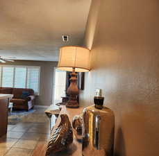 Living area with light tile patterned floors, ceiling fan, and a textured wall