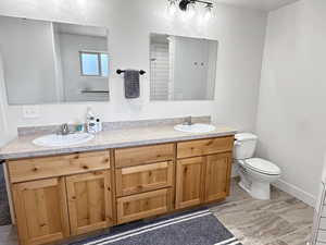 Full bath featuring double vanity, toilet, and baseboards