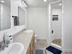 Full bathroom featuring tiled shower, double vanity, toilet, baseboards, and recessed lighting