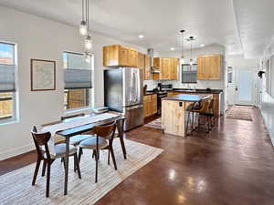 Kitchen featuring stainless steel appliances, a kitchen island, dark countertops, wall chimney exhaust hood, and finished concrete floors