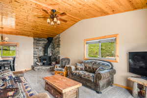 Living area featuring wood ceiling, a wood stove, vaulted ceiling, ceiling fan, and baseboards