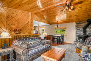 Living room with a ceiling fan, a wood stove, lofted ceiling, wooden ceiling, and carpet