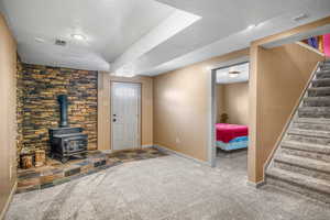 Unfurnished living room with a textured ceiling, carpet flooring, baseboards, stairway, and a wood stove