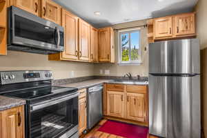 Kitchen featuring appliances with stainless steel finishes, a sink, open shelves, wood finished floors, and recessed lighting
