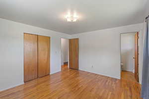 Unfurnished bedroom featuring light wood-style flooring, baseboards, a closet, and connected bathroom