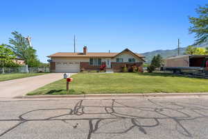 Ranch-style house featuring driveway, an attached garage, a chimney, a mountain view, and brick siding