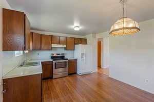 Kitchen featuring stainless steel electric stove, white refrigerator with ice dispenser, a sink, light countertops, and under cabinet range hood