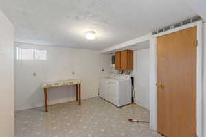 Laundry area with cabinet space, washing machine and dryer, light floors, and a textured ceiling