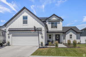 Modern farmhouse style home featuring board and batten siding, roof mounted solar panels, a front yard, and driveway